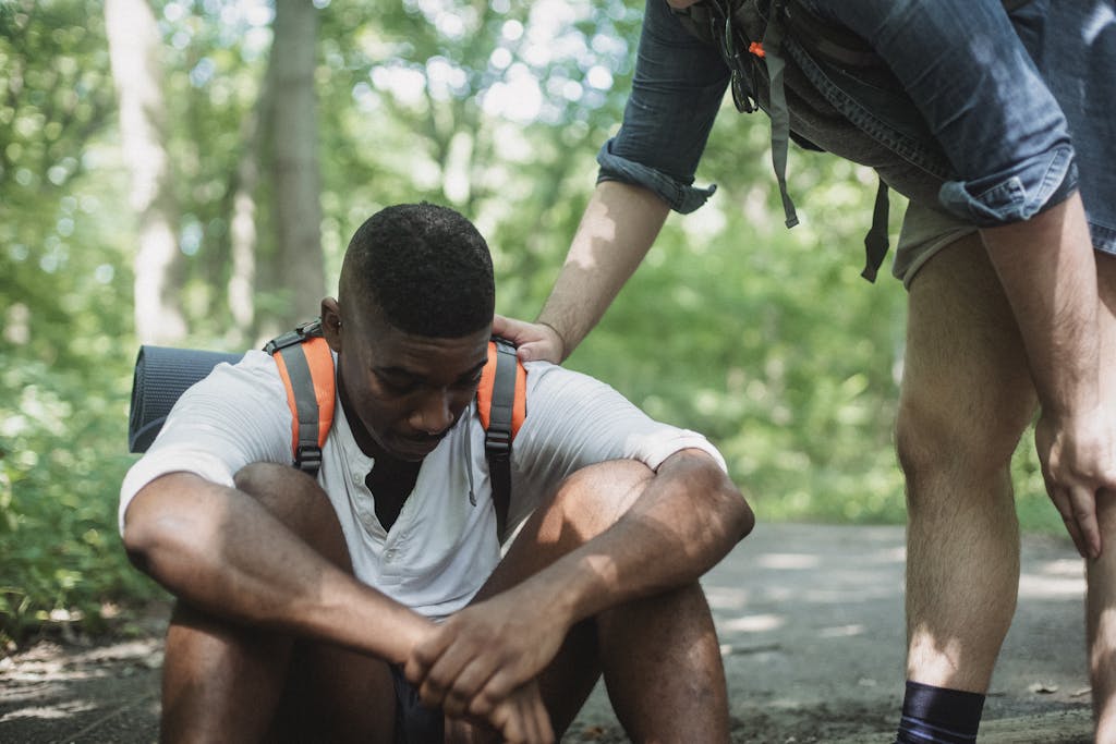 Unhappy black hiker sitting on ground in forest