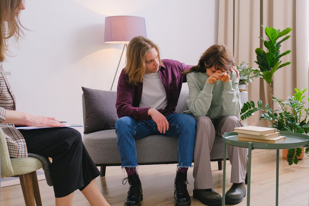 Young male embracing frustrated girlfriend during session with psychologist in light room in daytime